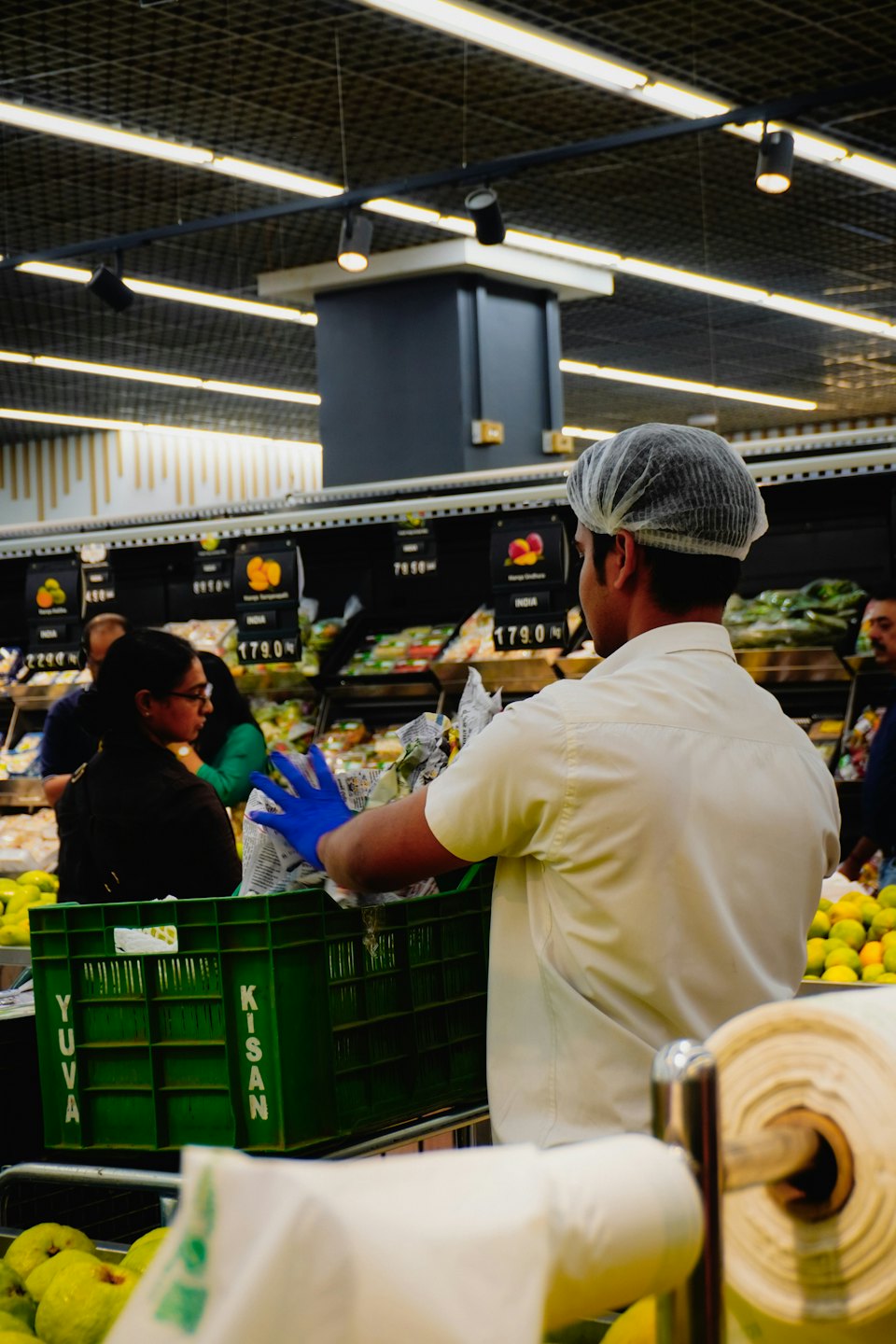 Employee restocks produce in a supermarket aisle.